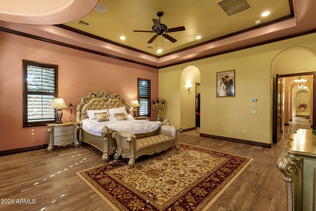 bedroom featuring arched walkways, wood finished floors, visible vents, ornamental molding, and a raised ceiling