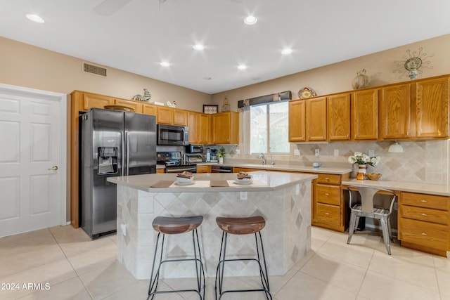 kitchen with light tile patterned flooring, backsplash, stainless steel appliances, a center island, and a breakfast bar area