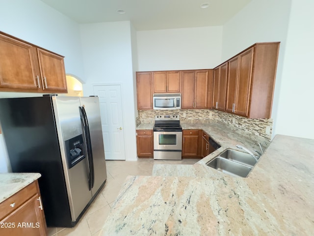 kitchen featuring brown cabinets, tasteful backsplash, appliances with stainless steel finishes, a sink, and light stone countertops