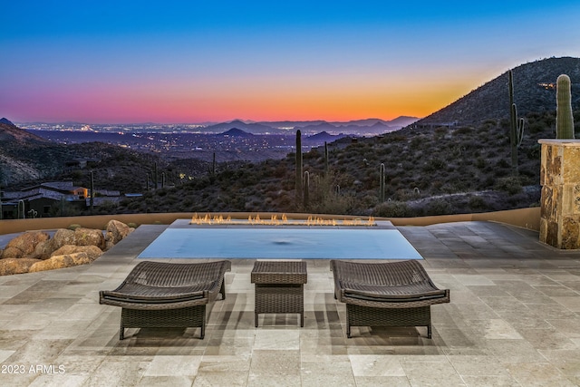 pool at dusk with outdoor lounge area, a patio, and a mountain view