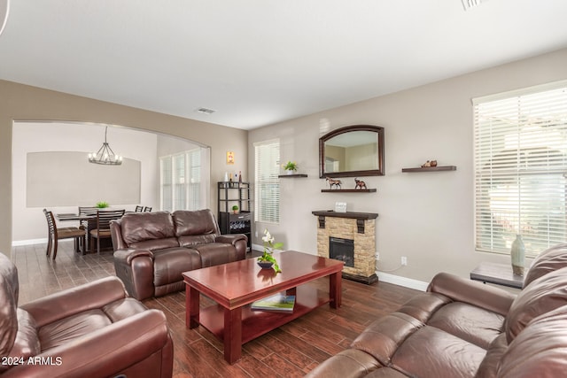 living room featuring a stone fireplace, plenty of natural light, and a notable chandelier