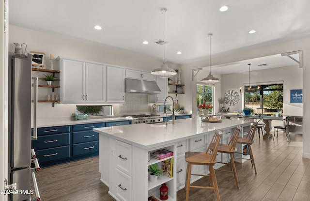 kitchen with white cabinets, hanging light fixtures, a kitchen island with sink, stainless steel refrigerator, and blue cabinets