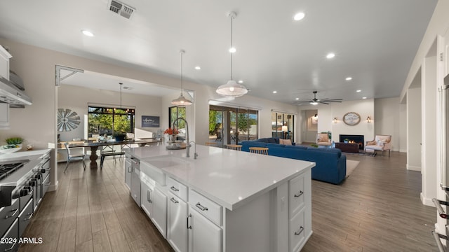 kitchen with ceiling fan, decorative light fixtures, sink, white cabinetry, and a kitchen island with sink