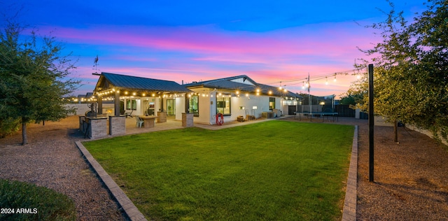 back house at dusk with a trampoline, area for grilling, a lawn, and a patio