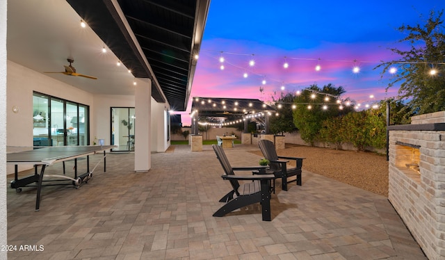 patio terrace at dusk with ceiling fan and exterior fireplace