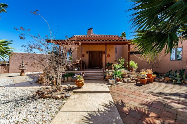 view of front of home with a tiled roof, a patio area, a chimney, and stucco siding