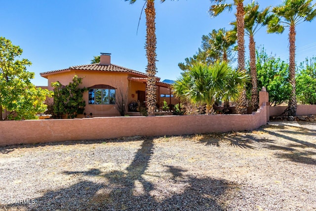 view of front of property with stucco siding, a chimney, fence, and a tiled roof