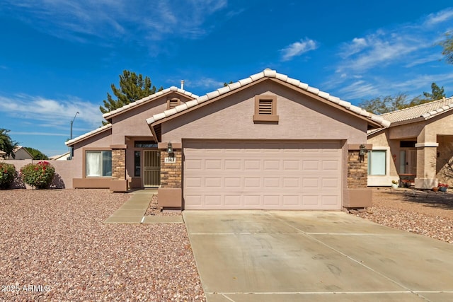 ranch-style house with a tile roof, stucco siding, concrete driveway, an attached garage, and stone siding