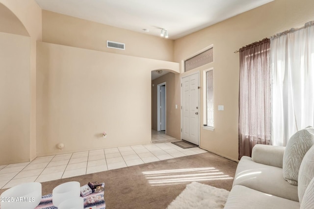 foyer featuring arched walkways, light tile patterned floors, visible vents, and light colored carpet