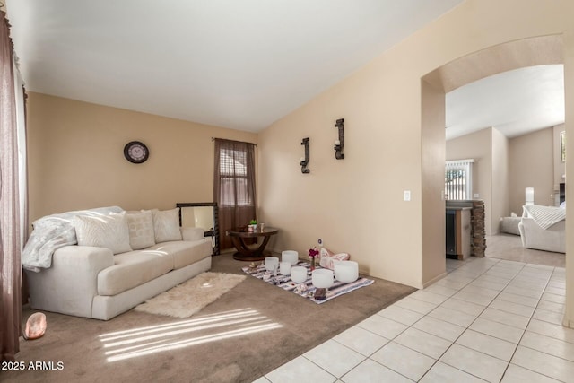 living room featuring arched walkways, light tile patterned flooring, vaulted ceiling, and light carpet
