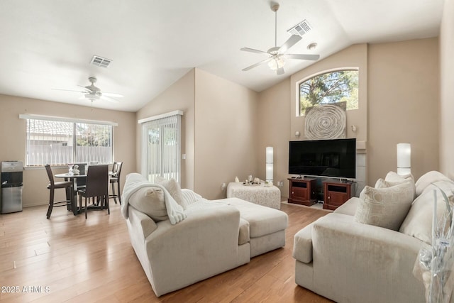 living room featuring light wood-type flooring, visible vents, vaulted ceiling, and a ceiling fan