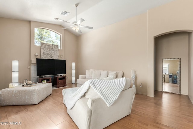 living room with arched walkways, light wood finished floors, visible vents, and a ceiling fan