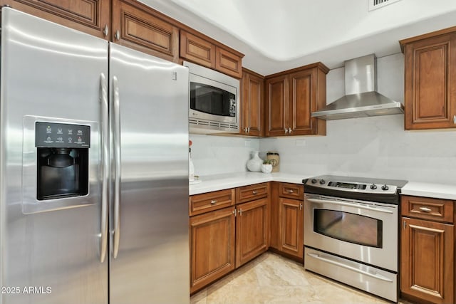kitchen with wall chimney range hood, light countertops, stainless steel appliances, and brown cabinets