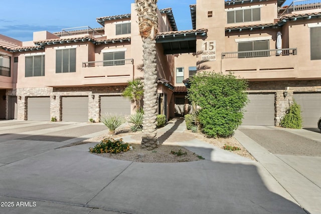 view of property featuring driveway, a tile roof, an attached garage, stone siding, and stucco siding