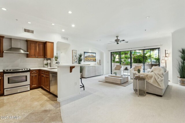 kitchen featuring stainless steel appliances, visible vents, wall chimney exhaust hood, and a peninsula