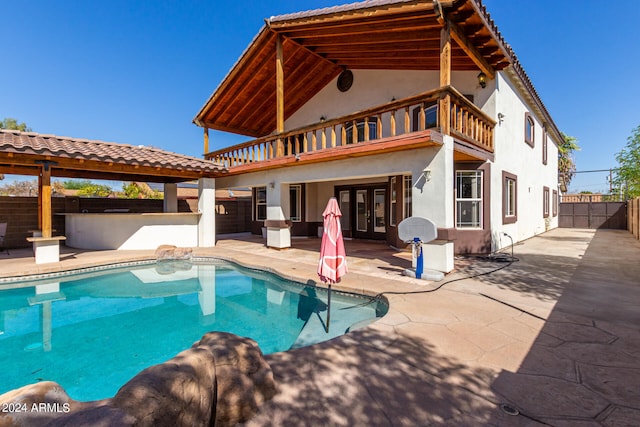 back of property featuring french doors, a pool with hot tub, a balcony, and a patio