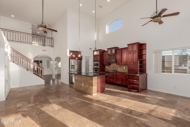 kitchen featuring a towering ceiling, decorative backsplash, a kitchen island with sink, and appliances with stainless steel finishes