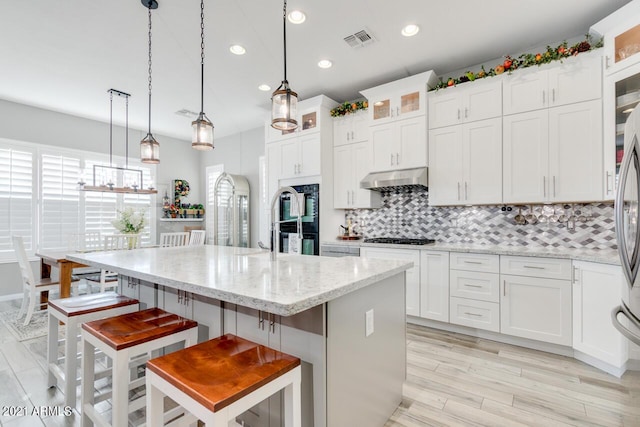 kitchen with decorative light fixtures, a center island with sink, visible vents, glass insert cabinets, and white cabinets