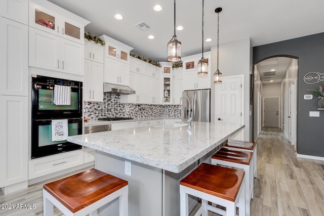 kitchen with glass insert cabinets, visible vents, an island with sink, and black appliances