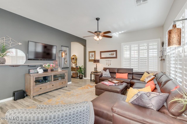 living room featuring light wood-type flooring, arched walkways, visible vents, and plenty of natural light