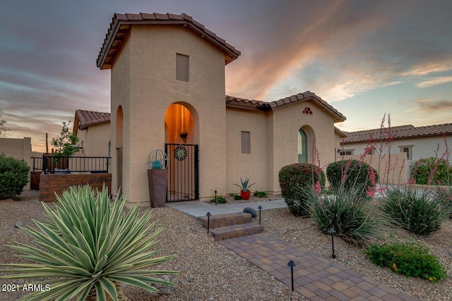 mediterranean / spanish-style house with a gate, a tile roof, and stucco siding