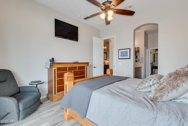 bedroom with visible vents, arched walkways, a ceiling fan, ensuite bathroom, and light wood-type flooring