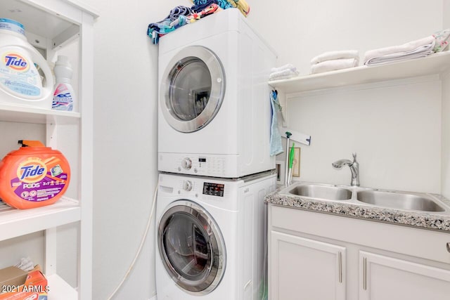 washroom featuring stacked washing maching and dryer, a sink, and cabinet space