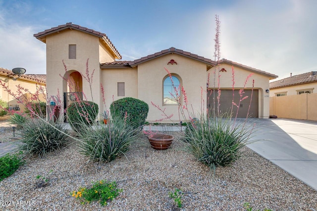 mediterranean / spanish-style house featuring stucco siding, concrete driveway, an attached garage, fence, and a tiled roof