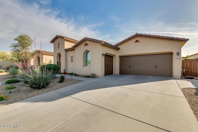 mediterranean / spanish home with driveway, an attached garage, a tiled roof, and stucco siding