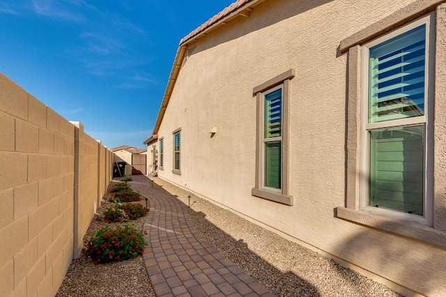 view of side of property with a tile roof, a fenced backyard, and stucco siding