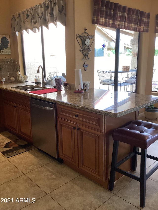 kitchen featuring a kitchen breakfast bar, stainless steel dishwasher, sink, stone counters, and light tile patterned flooring