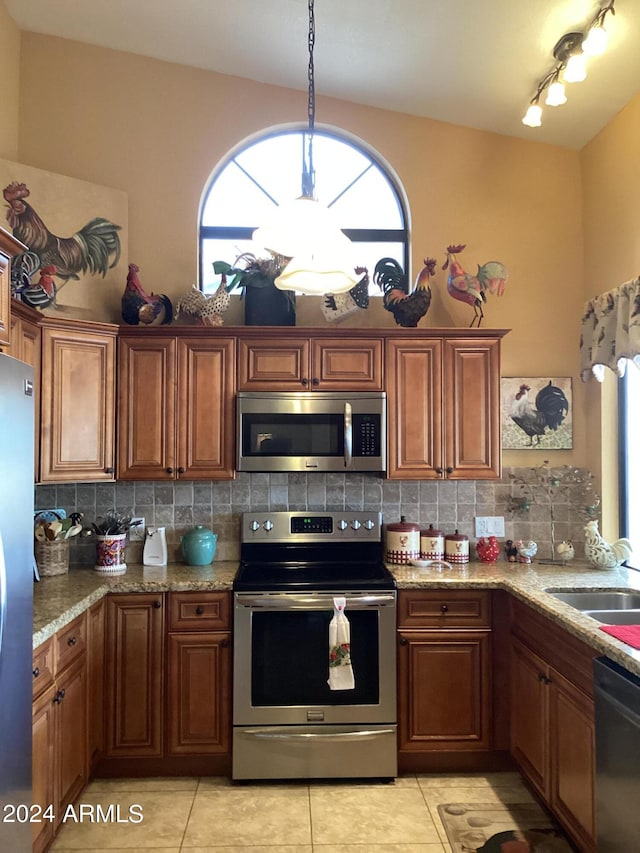 kitchen featuring stainless steel appliances, light stone countertops, tasteful backsplash, and decorative light fixtures