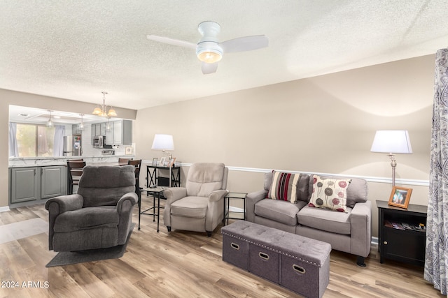 living room featuring a textured ceiling, ceiling fan with notable chandelier, and light wood-type flooring