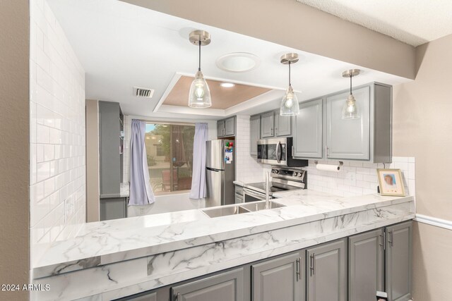 kitchen featuring tasteful backsplash, a raised ceiling, stainless steel appliances, decorative light fixtures, and gray cabinets