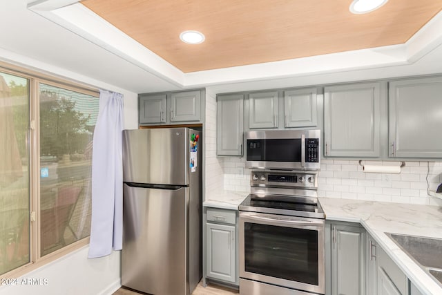 kitchen with gray cabinetry, stainless steel appliances, and a raised ceiling