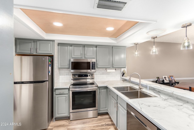 kitchen featuring a raised ceiling, appliances with stainless steel finishes, light hardwood / wood-style flooring, sink, and decorative light fixtures