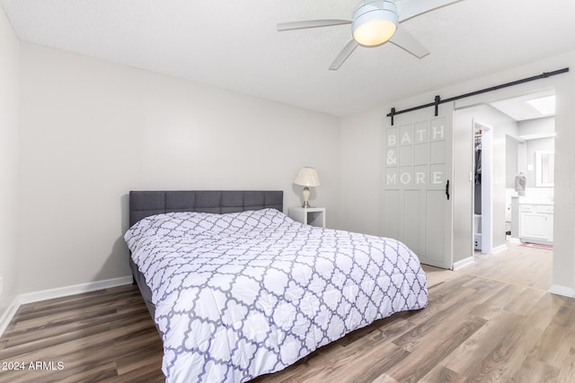 bedroom with ceiling fan, hardwood / wood-style flooring, a walk in closet, and a barn door