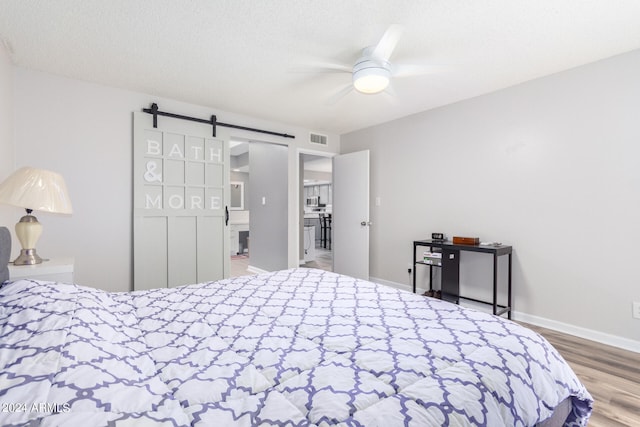 bedroom featuring hardwood / wood-style floors, a barn door, a textured ceiling, and ceiling fan