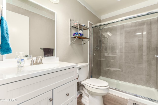 bathroom featuring a shower with door, hardwood / wood-style floors, toilet, vanity, and ornamental molding