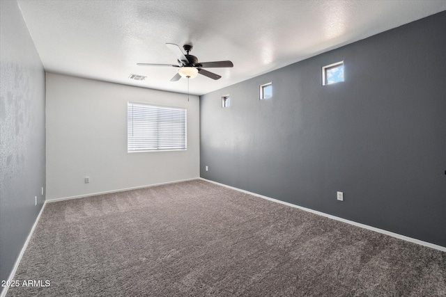 carpeted spare room with ceiling fan, baseboards, visible vents, and plenty of natural light