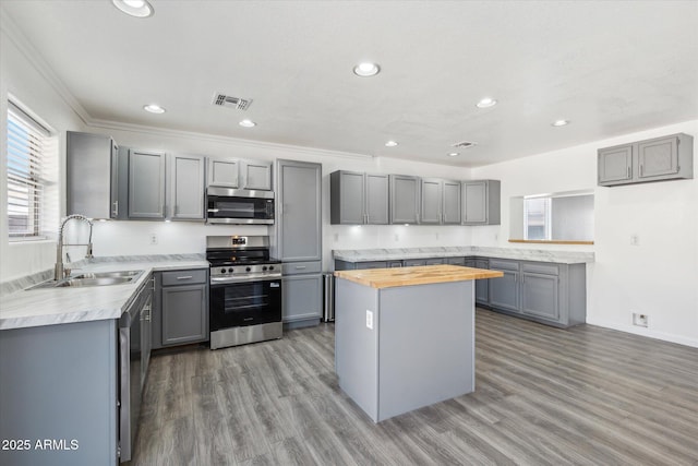 kitchen with visible vents, a sink, stainless steel appliances, wood counters, and gray cabinetry