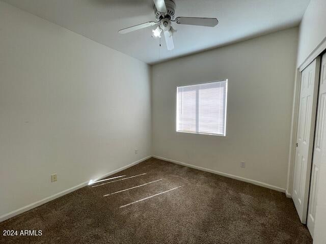 unfurnished bedroom featuring dark carpet, a closet, and ceiling fan