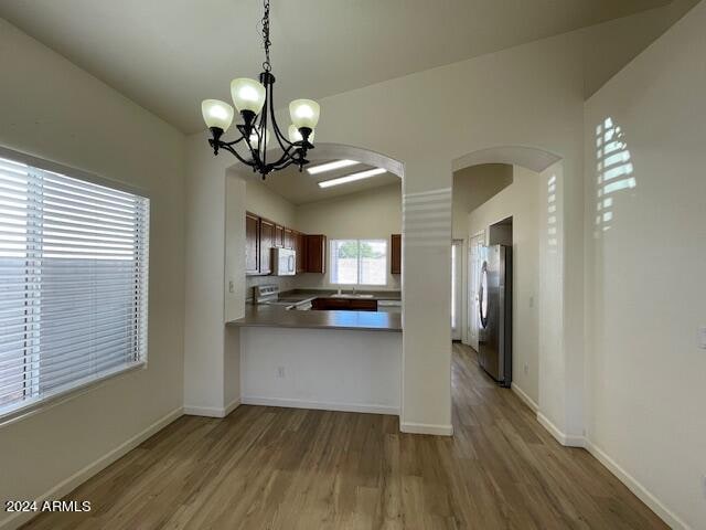 kitchen with range, a notable chandelier, wood-type flooring, and stainless steel refrigerator