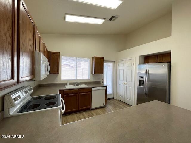 kitchen featuring white appliances, light hardwood / wood-style floors, high vaulted ceiling, and sink