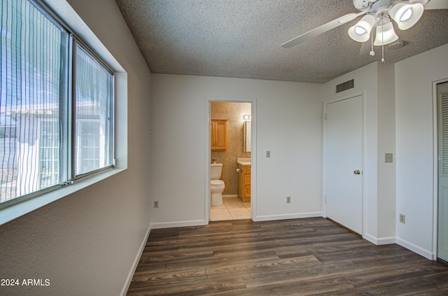 unfurnished bedroom with ensuite bathroom, a textured ceiling, dark hardwood / wood-style flooring, a closet, and ceiling fan