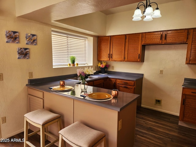 kitchen featuring dark wood-style floors, dark countertops, brown cabinets, and a peninsula