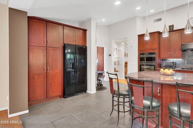 kitchen with a breakfast bar area, appliances with stainless steel finishes, hanging light fixtures, backsplash, and dark stone counters