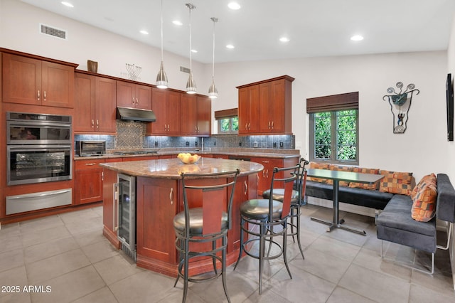 kitchen featuring pendant lighting, double oven, a kitchen breakfast bar, light stone countertops, and a kitchen island