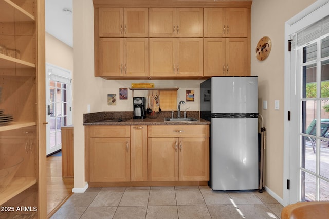 kitchen featuring sink, light tile patterned floors, stainless steel refrigerator, and dark stone counters