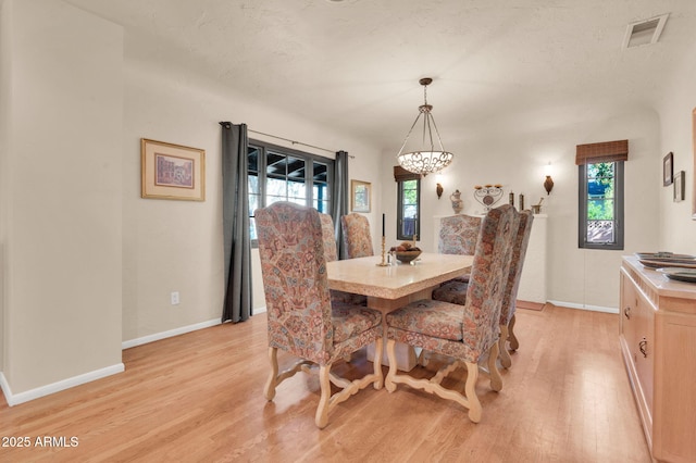 dining area with an inviting chandelier, light hardwood / wood-style floors, and a textured ceiling